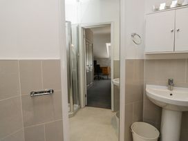 A bathroom with a pedestal sink and cabinet next to a shower room leading to a carpeted office with a desk and chair at Sunnycroft in Keswick