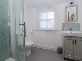 A bathroom with a shower, toilet, window with curtains, sink with cabinet, mirror, and soap dispenser at Sunnycroft in Keswick