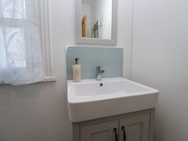 A bathroom sink with a soap dispenser a mirror above and a window with a sheer curtain at Sunnycroft in Keswick