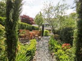 A garden with a gravel path leading to wooden outdoor furniture surrounded by green plants and trees at Sunnycroft in Keswick