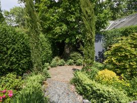 A garden path with gravel and stone surrounded by green shrubs and trees with a gray shed in the background at Sunnycroft in Keswick