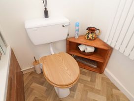 A toilet with a wooden seat and a shelf with a pitcher and toilet paper at Beehive in Beccles