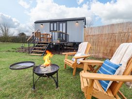 A small porch with a wooden table and chairs outside a shed with stairs and a fire pit in front of two wooden chairs with cushions and blankets at Shepherds Hut - Ash in Temple Bruer near Lincoln
