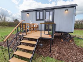 A shepherds hut with a wooden porch and stairs with outdoor furniture and lights at Shepherds Hut - Ash in Temple Bruer near Lincoln