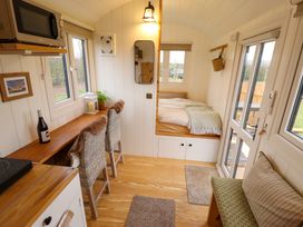 A small living space with a wooden counter and two wicker chairs a bed in a corner a microwave and a bottle on the counter at Shepherds Hut - Ash Temple Bruer near Lincoln