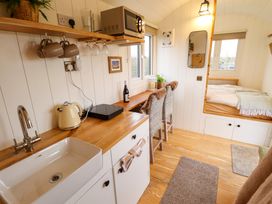 A compact kitchen and dining area with a sink kettle microwave two chairs and a built in bed at Shepherds Hut - Ash Temple Bruer near Lincoln