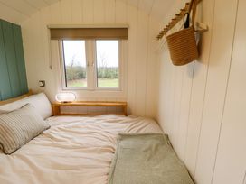 A bedroom with a double bed a small wooden side table a window and wall hooks with a bag at Shepherds Hut - Ash Temple Bruer near Lincoln