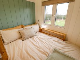 A bedroom with a bed under a window next to a small wooden shelf with a lamp at Shepherds Hut - Ash in Temple Bruer near Lincoln