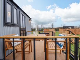 A wooden outdoor table with chairs and cushions on a deck attached to a small grey building at Shepherds Hut - Ash in Temple Bruer near Lincoln