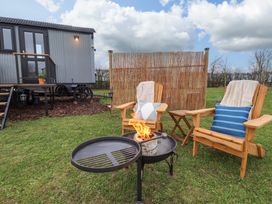 An outdoor seating area with two wooden chairs with cushions and blankets around a fire pit near a shepherds hut with a bamboo screen at Shepherds Hut - Ash in Temple Bruer near Lincoln