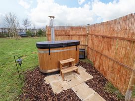 An outdoor wooden hot tub with steps on a paved area surrounded by mulch and fenced by bamboo panels at Shepherds Hut - Ash Temple Bruer near Lincoln