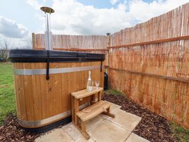 An outdoor wooden hot tub with a wooden step stool holding a bottle and glass at Shepherds Hut - Ash Temple Bruer near Lincoln