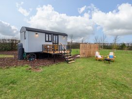 A shepherds hut with a small deck and stairs outside with two wooden chairs and a fire pit on grass at Shepherds Hut - Ash Temple Bruer near Lincoln