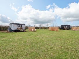Two small shepherd huts on a grassy field with wooden fences and outdoor seating at Shepherds Hut - Ash in Temple Bruer near Lincoln