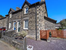 The exterior of a stone house with a blue door a small garden area and a wooden fence at Dola in Pentre Du near Betws-Y-Coed