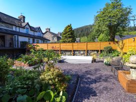 A garden with plants and shrubbery a wooden fence and stone houses in the background at Dola in Pentre Du near Betws-Y-Coed