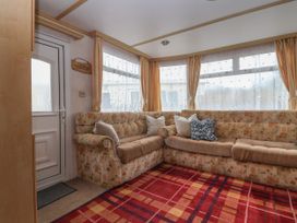 A corner seating area with patterned cushions and pillows next to windows with curtains in a caravan living space at Carnaby in South Chard