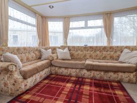 An L-shaped patterned sofa with cushions in front of large windows with curtains and a red checkered rug on the floor at Carnaby in South Chard