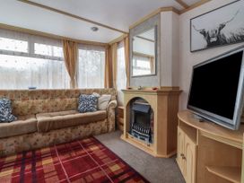 A living room with a patterned sofa a fireplace a wall mirror a television on a wooden stand and a red checked rug at Carnaby in South Chard