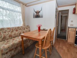 A dining area with a wooden table two chairs a patterned sofa and a window with curtains at Carnaby in South Chard