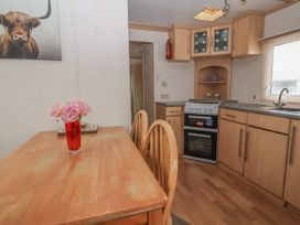 A kitchen with wooden cabinets a stove a sink and a wooden dining table with chairs and a vase of flowers on the table at Carnaby in South Chard
