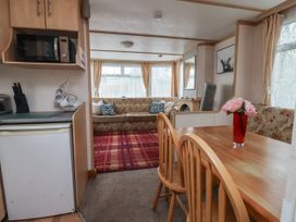 A dining area with a wooden table and chairs next to a kitchen with a microwave and fridge and a living room with sofas and a red rug at Carnaby South Chard