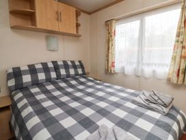 A bedroom with a bed with checkered bedding beside a window with curtains and a wall cabinet at Carnaby in South Chard
