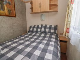 A bedroom with a bed with gray and white checkered bedding a wooden cabinet above and a window with patterned curtains at Carnaby in South Chard