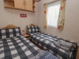 A bedroom with two single beds with checkered bedding a window with curtains and a wooden cabinet above the beds at Carnaby in South Chard