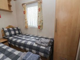 A bedroom with two single beds with checkered bedding a wooden wardrobe and a window with curtains at Carnaby in South Chard