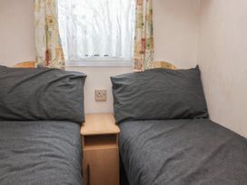 A small bedroom with two single beds and a nightstand under a window with patterned curtains at Carnaby South Chard