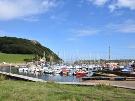 A marina with multiple sailboats and motorboats docked near a grassy hill and stone wall at Carnaby in South Chard