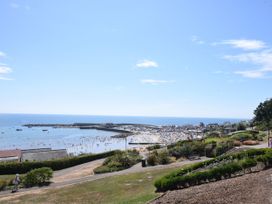 A coastal view with a beach, people on the sand and in the water, boats in a harbor, and a grassy park area with pathways and benches at Carnaby in South Chard