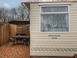 Exterior of a caravan with a window and outdoor table with umbrella and chairs at Carnaby in South Chard