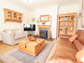 A living room with a leather sofa a beige armchair wooden shelves and a wood stove at Mor Iwerddon in Barmouth