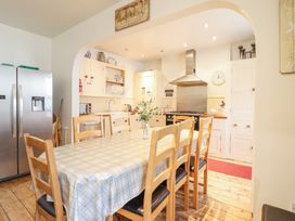 A kitchen and dining area with a wooden table and chairs a refrigerator and cabinets at Mor Iwerddon in Barmouth