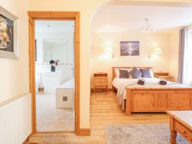 A bedroom with a wooden bed and bedside tables next to a doorway leading to a bathroom at Mor Iwerddon in Barmouth