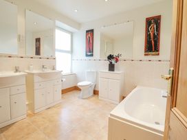 A bathroom with two sinks, a toilet, a bathtub, mirrors, and artwork on the walls at Mor Iwerddon in Barmouth