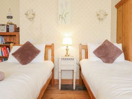 A bedroom with two single wooden beds a white nightstand with a lamp and bookshelf at Mor Iwerddon in Barmouth
