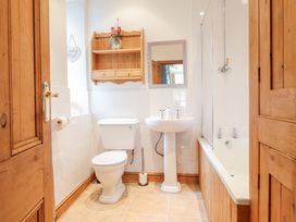 A bathroom with a toilet pedestal sink wooden shelves and a bathtub with a glass screen at Mor Iwerddon in Barmouth