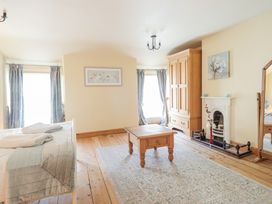 A bedroom with a wooden table, wardrobe, fireplace, mirror, and two windows with curtains at Mor Iwerddon in Barmouth