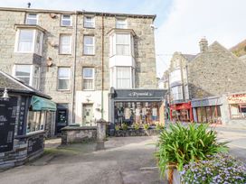 A stone building with shops including Pyramid clothing store and a donut shop with plants in the foreground at Mor Iwerddon in Barmouth