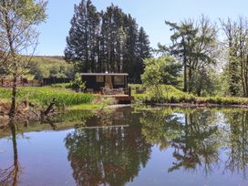 A small cabin with a deck and outdoor furniture near a pond surrounded by trees and vegetation at Celyn in Bontddu near Dolgellau