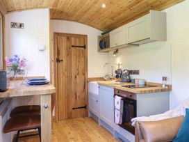 A small kitchen with wooden ceiling and floor with a door a countertop with sink kettle and oven with a brown chair at Celyn Bontddu near Dolgellau