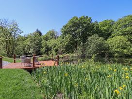 A wooden deck with four chairs overlooking a pond surrounded by tall green plants and trees at Celyn in Bontddu near Dolgellau