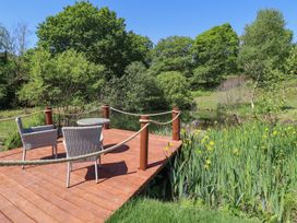 A wooden deck with two chairs and a table overlooking a pond with trees and yellow flowers at Celyn in Bontddu near Dolgellau