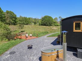 An outdoor area with a wooden hot tub gravel path fire pit and seating deck near a black building at Celyn in Bontddu near Dolgellau