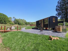 A small black cabin on wheels with steps and a bench near a wooden hot tub and a dog lying on grass at Celyn in Bontddu near Dolgellau