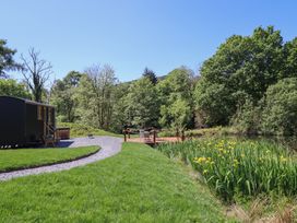A grassy garden with a gravel path leading to a wooden deck with chairs and yellow flowers near trees at Celyn in Bontddu near Dolgellau
