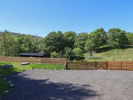 An outdoor scene with a gravel area a wooden fence a red gate and trees at Celyn in Bontddu near Dolgellau